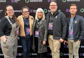 Johnson, Cristiano, Traister, Crabtree-Ireland and Aguirre stand against a black Denver Film and SeriesFest step-and-repeat backdrop. All wear casual clothing and lanyards with colorful badges.